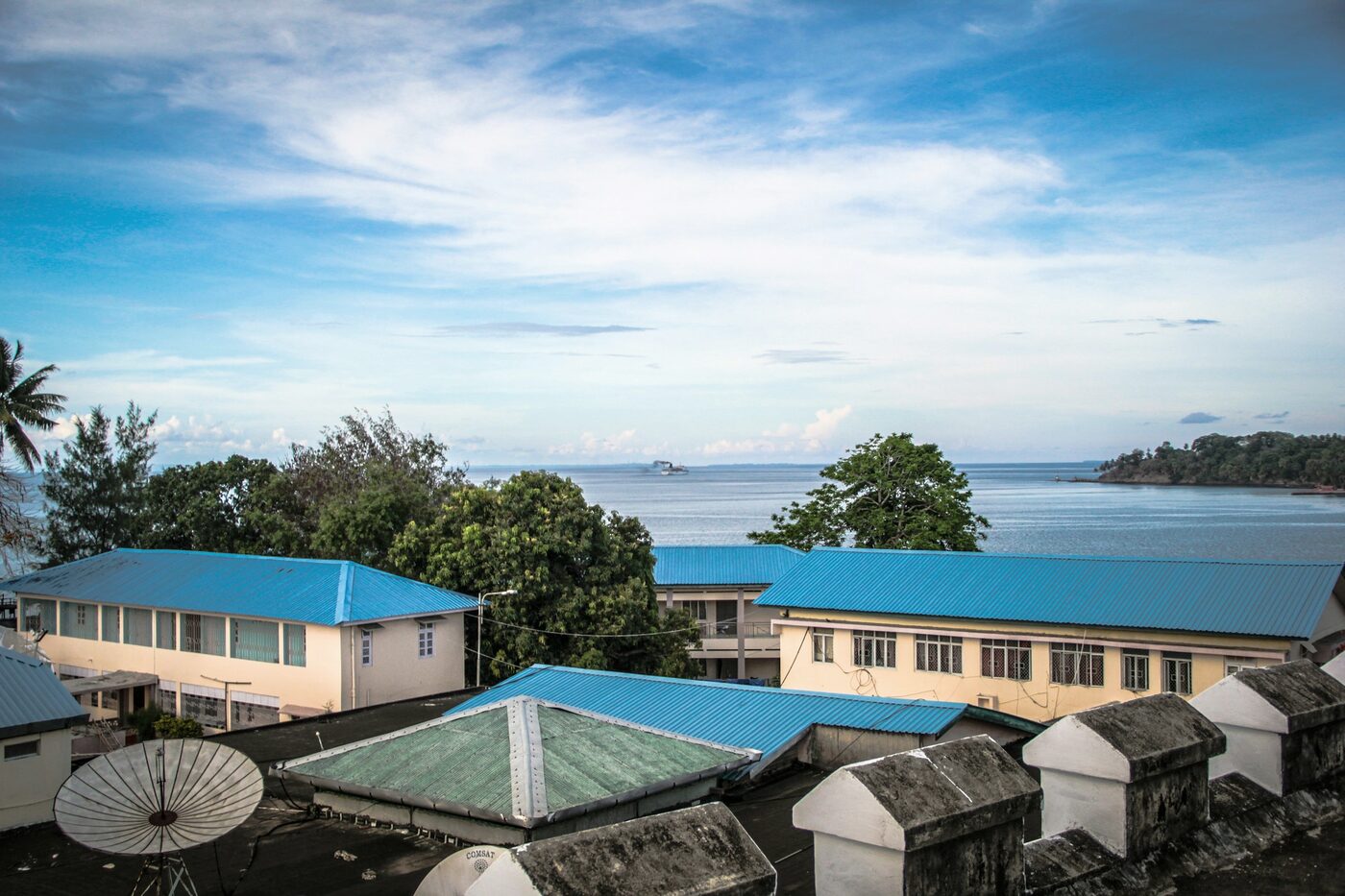 Blue-roofed school buildings beside the sea under a wide Pacific sky